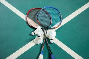 Badminton rackets and white cream badminton shuttlecocks after playing or after games on green floor in indoor badminton court, soft focus, concept for badminton lovers around the world. photo