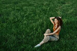 A woman enjoying the outdoors sitting in the park on the green grass in her casual clothes lit by the bright summer sun without mosquitoes photo