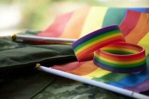 arco iris bandera y arco iris pulseras en camuflaje fondo, concepto para celebraciones de lgbt personas en orgullo mes alrededor el mundo, suave y selectivo atención en pulsera. foto