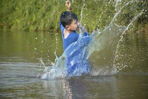 Asian boy in blue t-shirt is spending his freetimes by diving, swimming, throwing rocks and catching fish in the river happily, hobby and happiness of children concept, in motion. photo