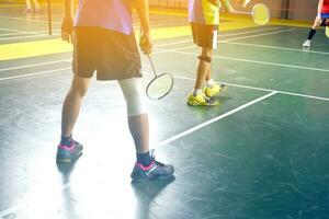 un bádminton atleta envuelve su Derecha rodilla con un blanco rodilla vendaje a apoyo su rodilla y sanar su lesión mientras jugando bádminton juntos con su amigos en el bádminton corte. foto