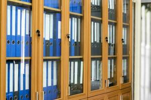 Wooden and glass office binders cabinet that hold a large number of binders in an office to keep and store the data of the company, soft and selective focus on document binders. photo