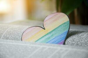 Closeup view of bookmark in heart shape which drew with rainbow colours, blurred opened old book background, concept for calling out all people to respect gender diversity of humans in pride month. photo