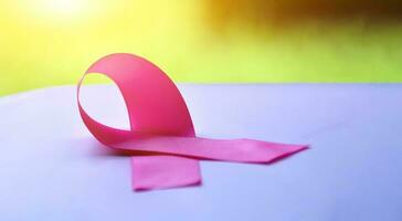rosado cintas en de madera mesa, luz de sol y borroso fondo, concepto para pecho cáncer conciencia alrededor el mundo. suave y selectivo atención en rosado cintas foto
