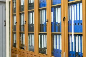 Wooden and glass office binders cabinet that hold a large number of binders in an office to keep and store the data of the company, soft and selective focus on document binders. photo