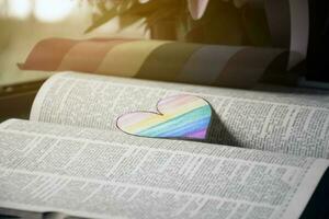 Closeup view of bookmark in heart shape which drew with rainbow colours, blurred opened old book background, concept for calling out all people to respect gender diversity of humans in pride month. photo