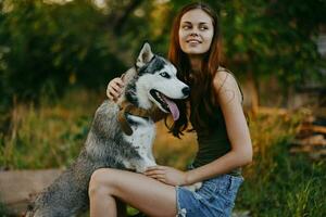 un mujer con un fornido raza perro sonrisas y afectuosamente golpes su amado perro mientras caminando en naturaleza en el parque en otoño en contra el fondo de puesta de sol foto