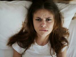 mujer con un enojado expresión picaduras su labio mientras acostado en cama parte superior ver foto