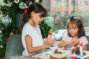 dos pequeño hermanas teniendo divertido mientras haciendo Navidad natividad artesanía con a hogar - real familia foto