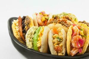 Arepas with assorted fillings served in a black ceramic dish on white background photo