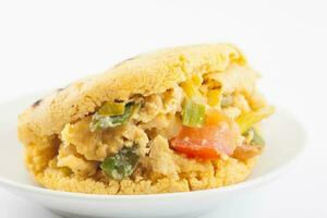 Arepas filled with scrambled eggs served in a white dish on white background photo