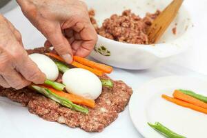 preparación de un horneado huevo y vegetales relleno pastel de carne cubierto con tocino. carne rodar foto