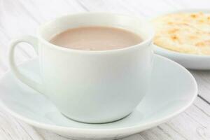 Cup of hot chocolate with cheese and arepa served in white dishware photo