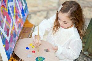 Little blonde girl painting outdoors photo