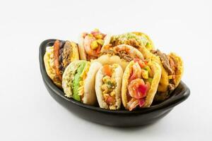 Arepas with assorted fillings served in a black ceramic dish on white background photo