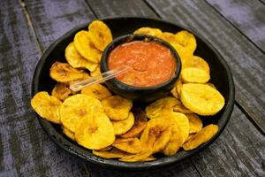 Plantain chips served with Colombian traditional hogao on top of a wooden table photo