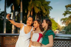 Tourists taking a selfie in one of the bridges along the Cali River Boulevard with La Ermita church on background in the city of Cali in Colombia. Mother and teenager daughters traveling concept. photo