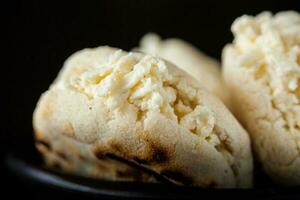 Colombian traditional white corn arepa stuffed with grated cheese in a black ceramic dish on black background photo