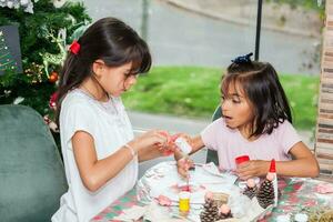 dos pequeño hermanas teniendo divertido mientras haciendo Navidad natividad artesanía con a hogar - real familia foto