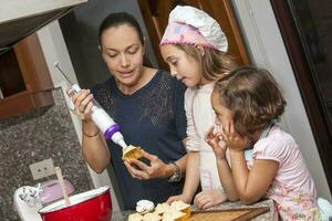 Mother and daughters having fun in the kitchen baking together. Preparing cupcakes with mom photo
