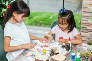 dos pequeño hermanas teniendo divertido mientras haciendo Navidad natividad artesanía con a hogar - real familia foto