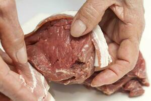 Wrapping beef tenderloin medallion with pork bacon. Filet mignon photo