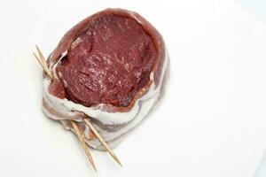 Raw beef tenderloin medallion wrapped in pork bacon. Filet mignon preparation. photo
