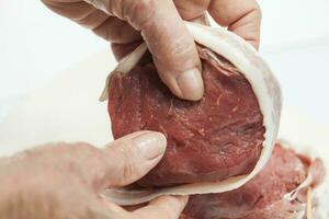 Wrapping beef tenderloin medallion with pork bacon. Filet mignon photo