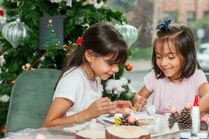 dos pequeño hermanas teniendo divertido mientras haciendo Navidad natividad artesanía con a hogar - real familia foto