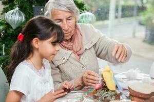 Little girl having fun while making christmas Nativity crafts with her grandmother - Real family photo