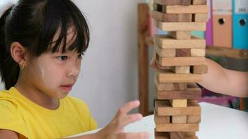 schattig Aziatisch broers en zussen hebben pret spelen jenga samen. twee kinderen spelen jenga bord spel Aan tafel in kamer Bij huis. houten puzzels zijn spellen dat toenemen intelligentie- voor kinderen. video