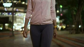 fêmea atleta dentro encapuzado camisa andar às noite cidade ruas com grande quantidade do luzes dentro a fundo. video