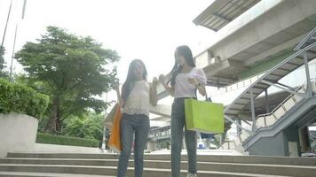 two women shopping goods outdoor in department store. Attractive young female friend holding shopping bags then walking with happiness enjoy purchasing in shopping mall center together video
