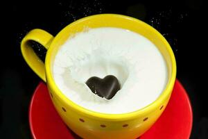 Chocolate heart falling and splashing into a cup full of milk. photo