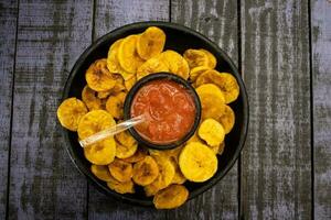 Plantain chips served with Colombian traditional hogao on top of a wooden table photo