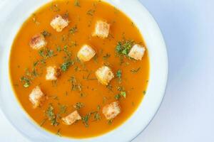 Pumpkin soup with croutons served in a white dish photo