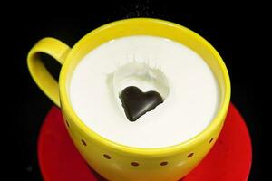 chocolate corazón que cae y salpicaduras dentro un taza lleno de leche. foto