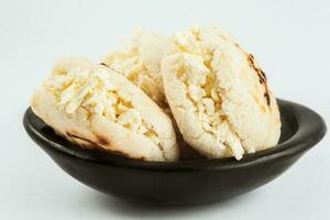 Colombian traditional white corn arepa stuffed with grated cheese in a black ceramic dish on white background photo