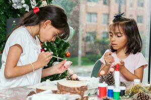 dos pequeño hermanas teniendo divertido mientras haciendo Navidad natividad artesanía con a hogar - real familia foto