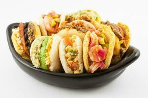 Arepas with assorted fillings served in a black ceramic dish on white background photo