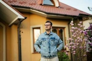 retrato de elegante hombre en lentes y pantalones chaqueta planteado en contra su casa. foto