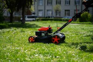 Communal services gardener worker man using lawn mower for grass cutting in city park. photo