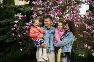 contento familia con dos hijas disfrutando bonito primavera día cerca magnolia floreciente árbol. foto