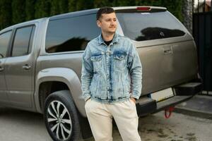 Man in jeans jacket stand against gray pick up suv car truck. photo