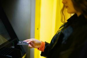 Young brunette girl withdrawing money from credit card at yellow ATM. photo