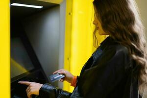 Young brunette girl withdrawing money from credit card at yellow ATM. photo