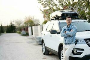 hombre en pantalones chaqueta en pie cerca blanco americano suv coche con techo estante caja. foto