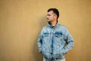 Side portrait of stylish man in jeans jacket against yellow wall. photo