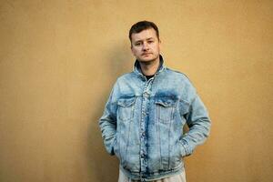 Portrait of stylish man in jeans jacket against yellow wall. photo
