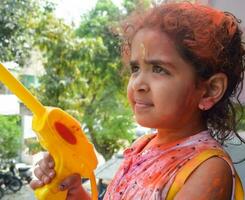 Sweet little Indian girl playing colours on Holi festival, holding pichakaree full of colours, Holi festival celebrations in Delhi, India photo